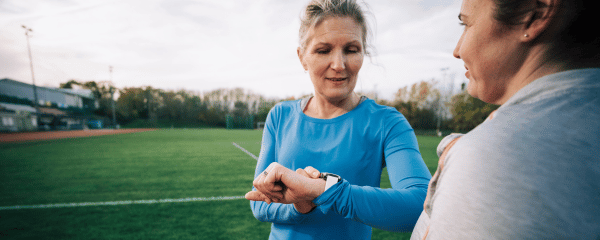 Female athlete in a blue t shirt checking their sports watch at the running track before a workout on a sunny day