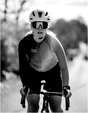 Female cyclist standing up out of the saddle cycling up a hill in black and white